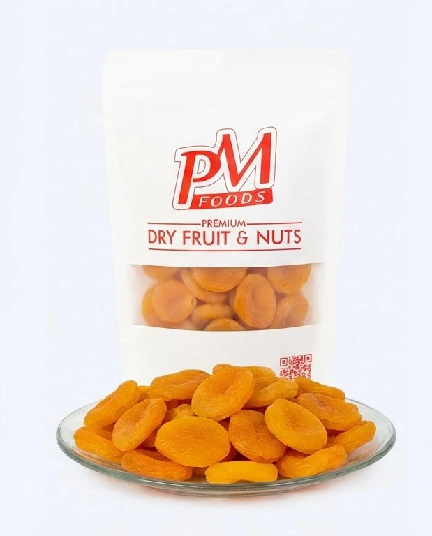 Bag of PM Foods premium dry fruit and nuts with a plate of apricots on a white background

